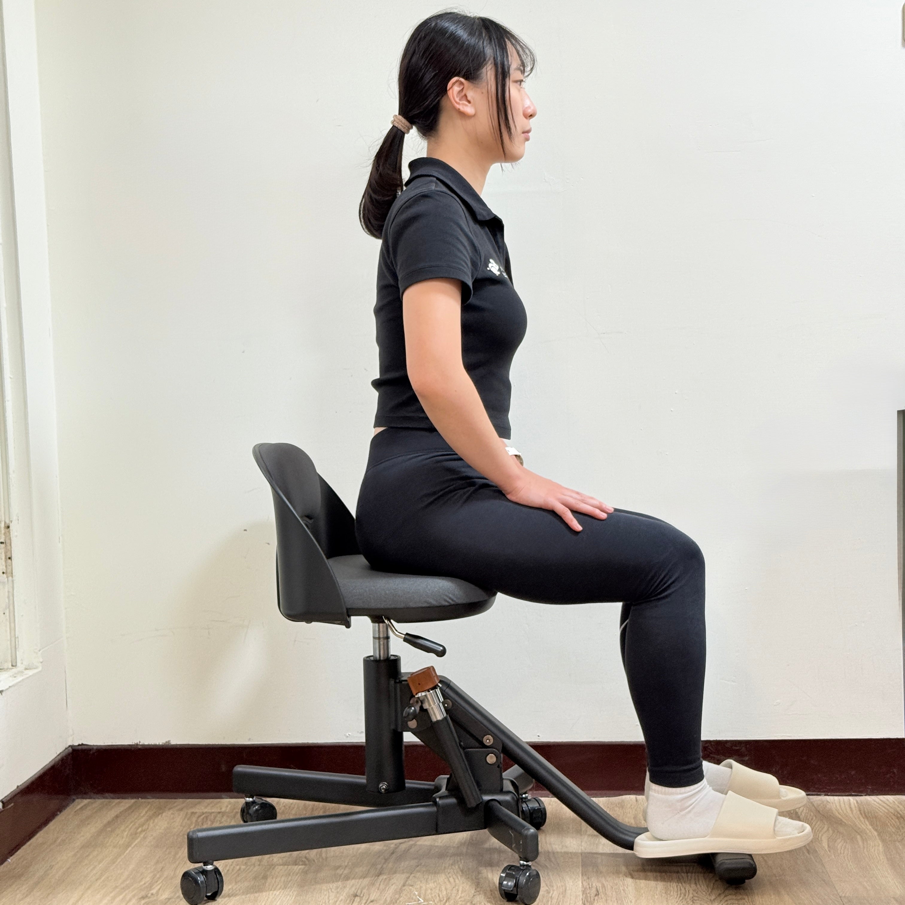 女性側坐於 Wonder Core Chaircise 核心喚醒工學椅、雙腳踩底部踏板，示範駝背矯正的正確坐姿辦公姿勢