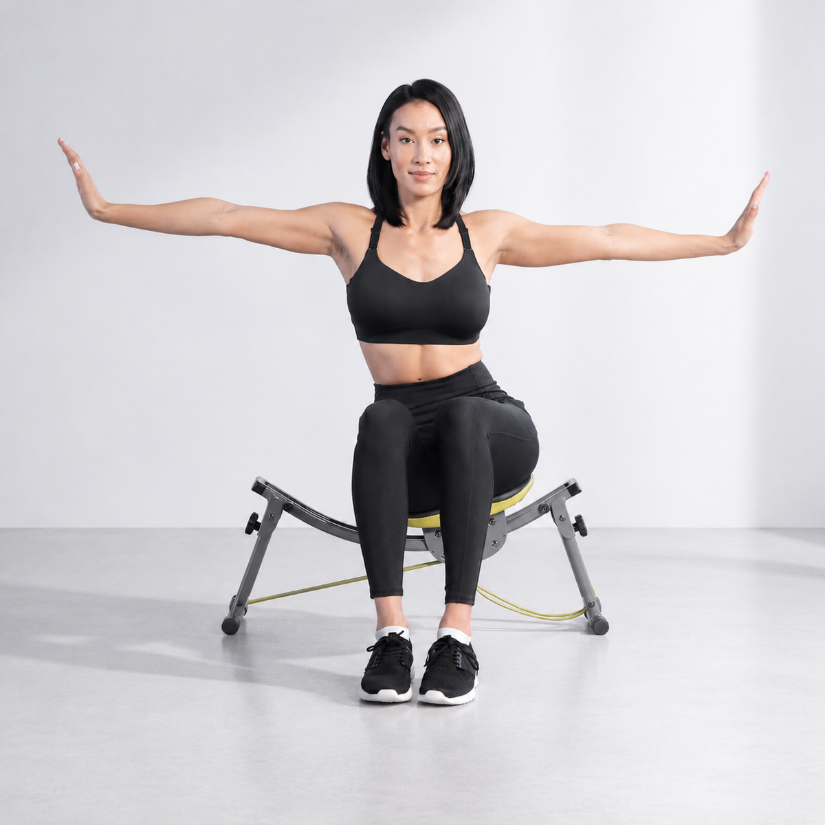 女性穿黑色運動服坐在 Wonder Core Sway N Fit 搖擺健腹椅上、雙臂向兩側平伸保持平衡，示範久坐上班族在家做的低衝擊坐姿核心喚醒訓練